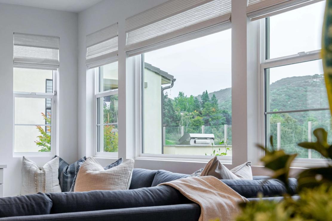Bright living room with large white-framed windows overlooking green hills, showcasing stylish and energy-efficient replacement windows and doors Corona, CA for improved comfort and natural light.