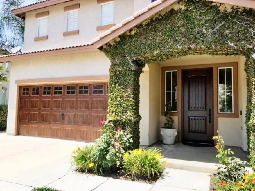Front exterior of a two-story home with a wooden garage door, updated entry door, and decorative windows, highlighting quality replacement windows and doors Corona, CA for enhanced curb appeal and durability.